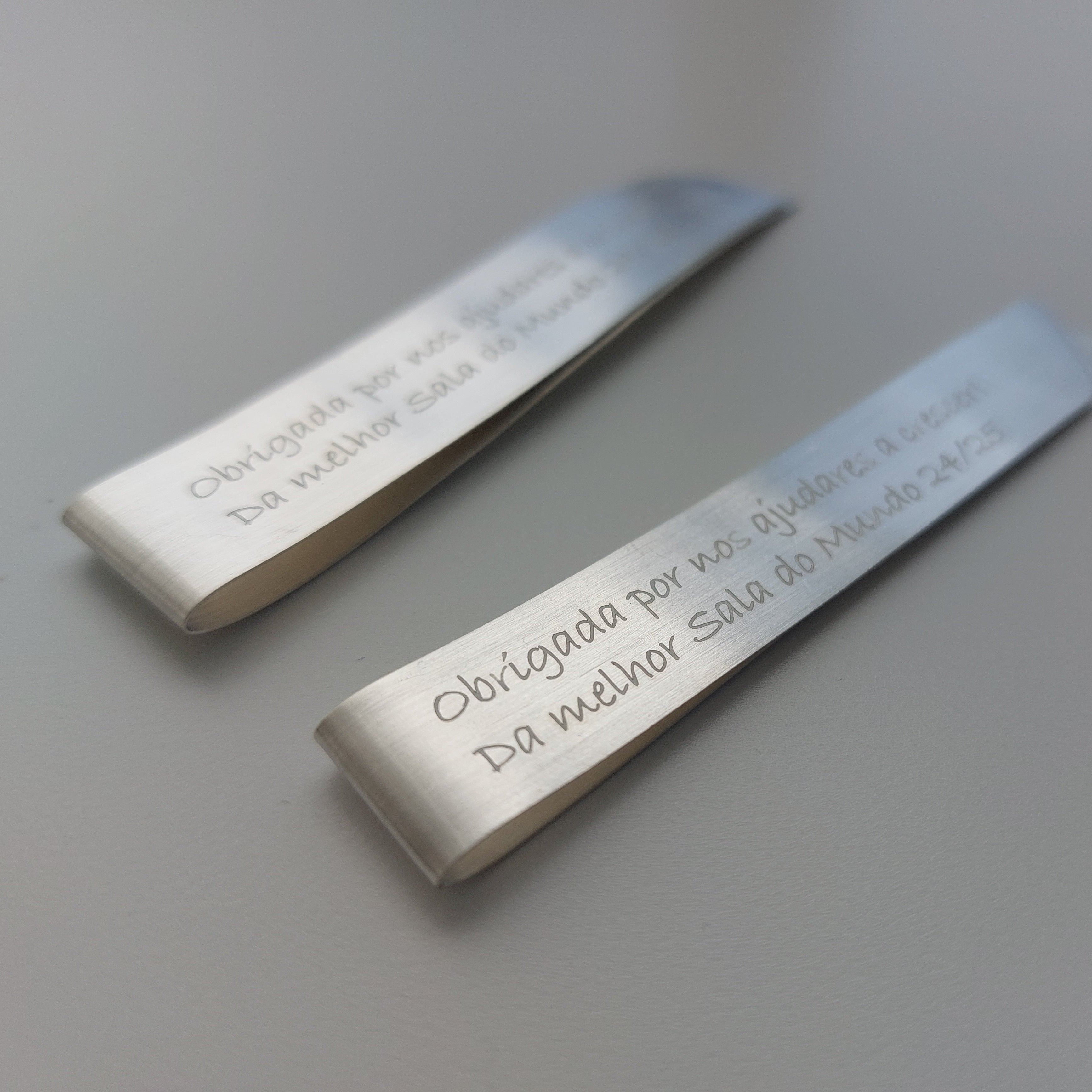 Two metallic bookmarks with engraved text on a light gray background