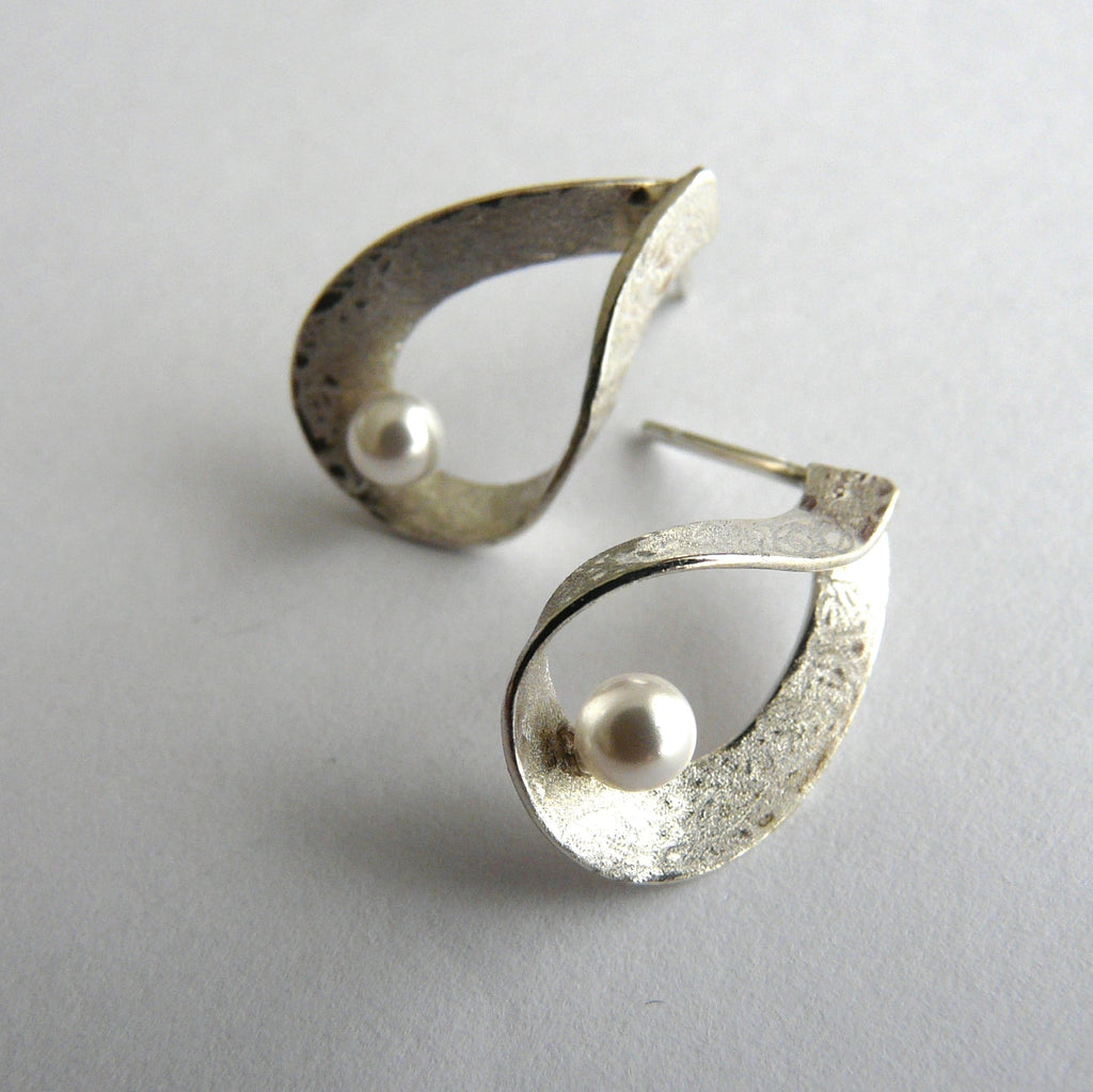Pair of silver earrings with a pearl center on a light gray background