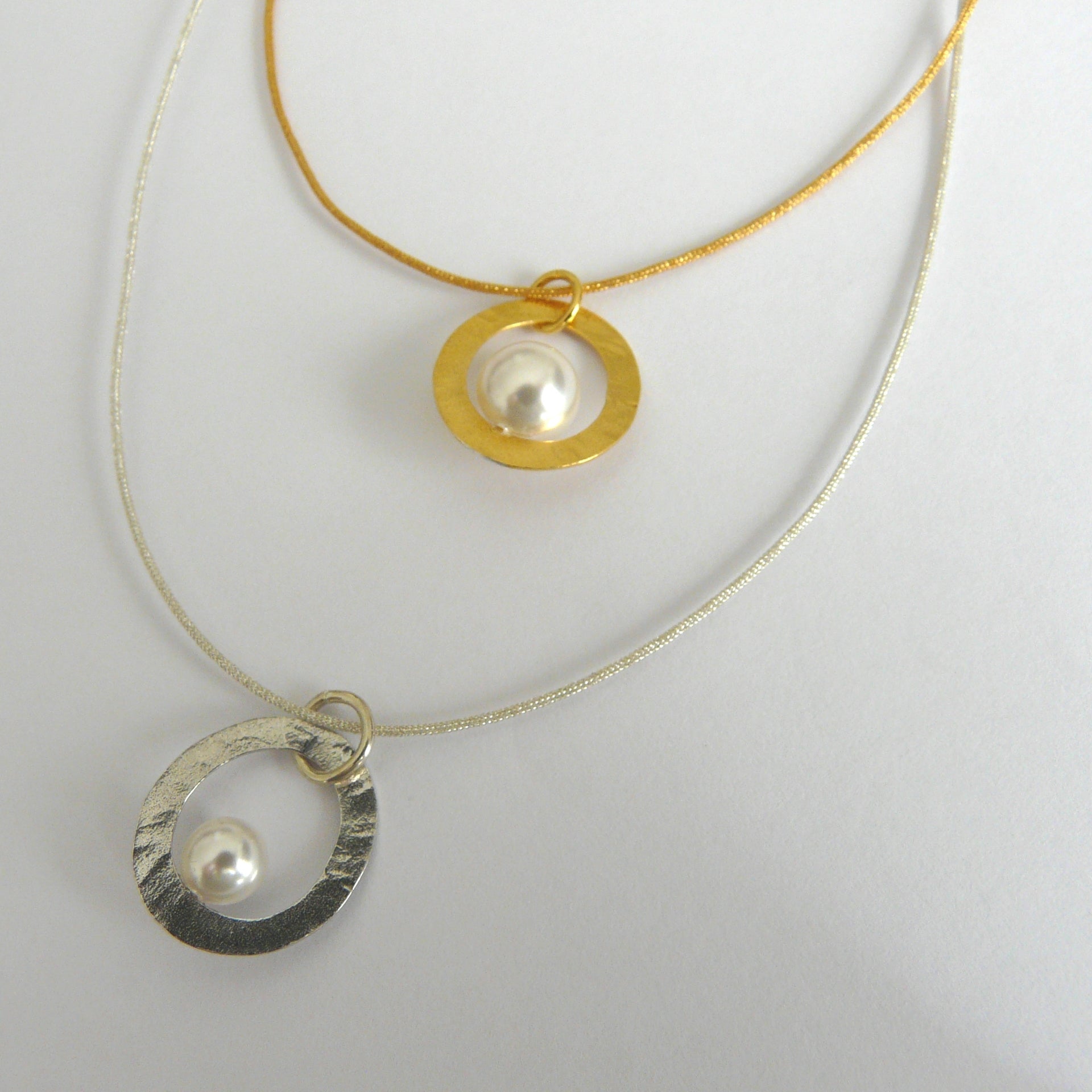 Two necklaces with circular pendants featuring pearls on a white background