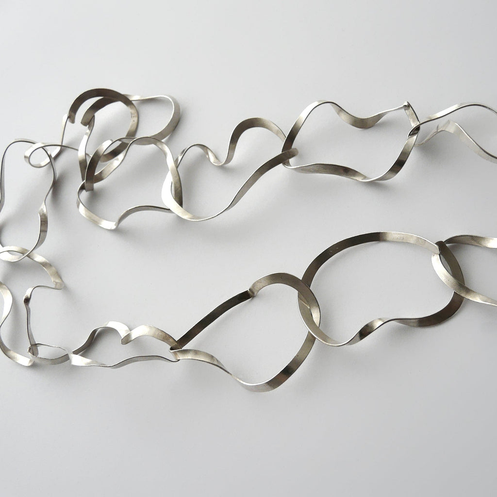 Silver necklace with wavy design on a light gray background