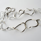 Silver necklace with wavy design on a light gray background