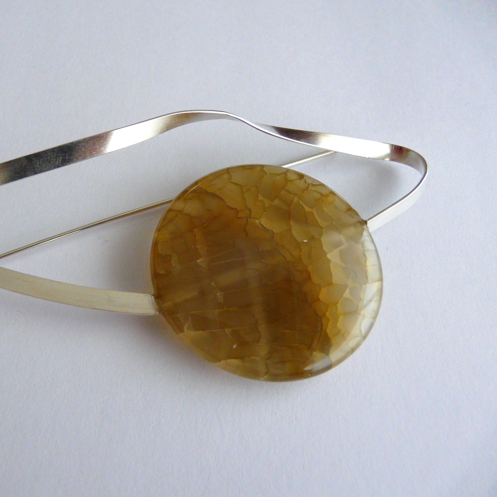 Gold bracelet with a large amber-colored stone on a light gray background