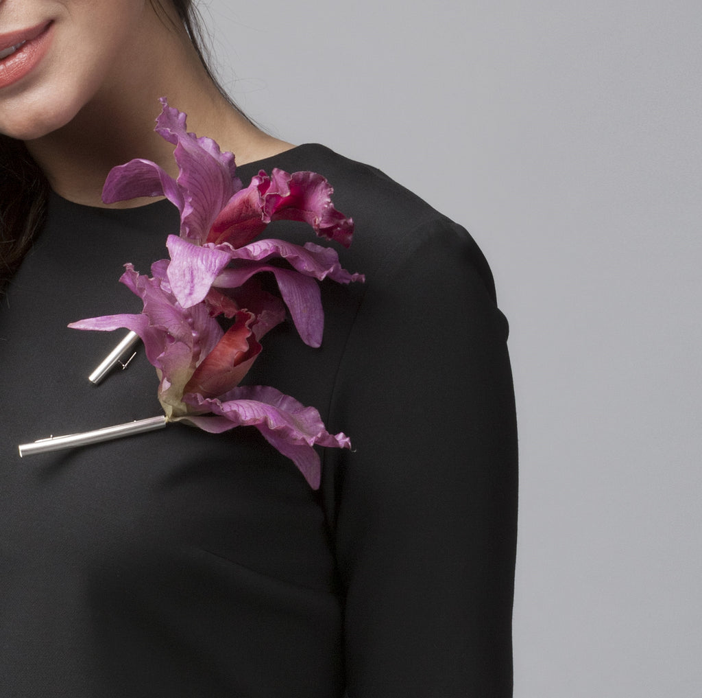 Close-up of a pink flower brooch on a black garment against a gray background