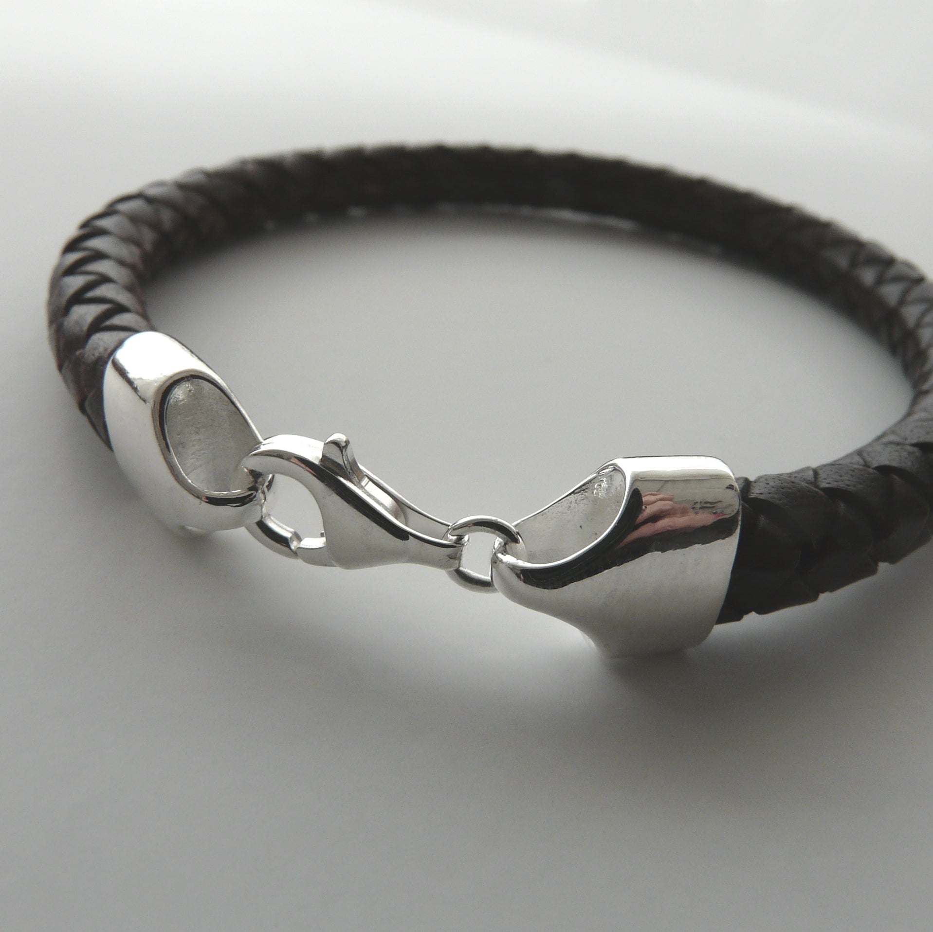 Black braided leather bracelet with a silver clasp on a light gray background