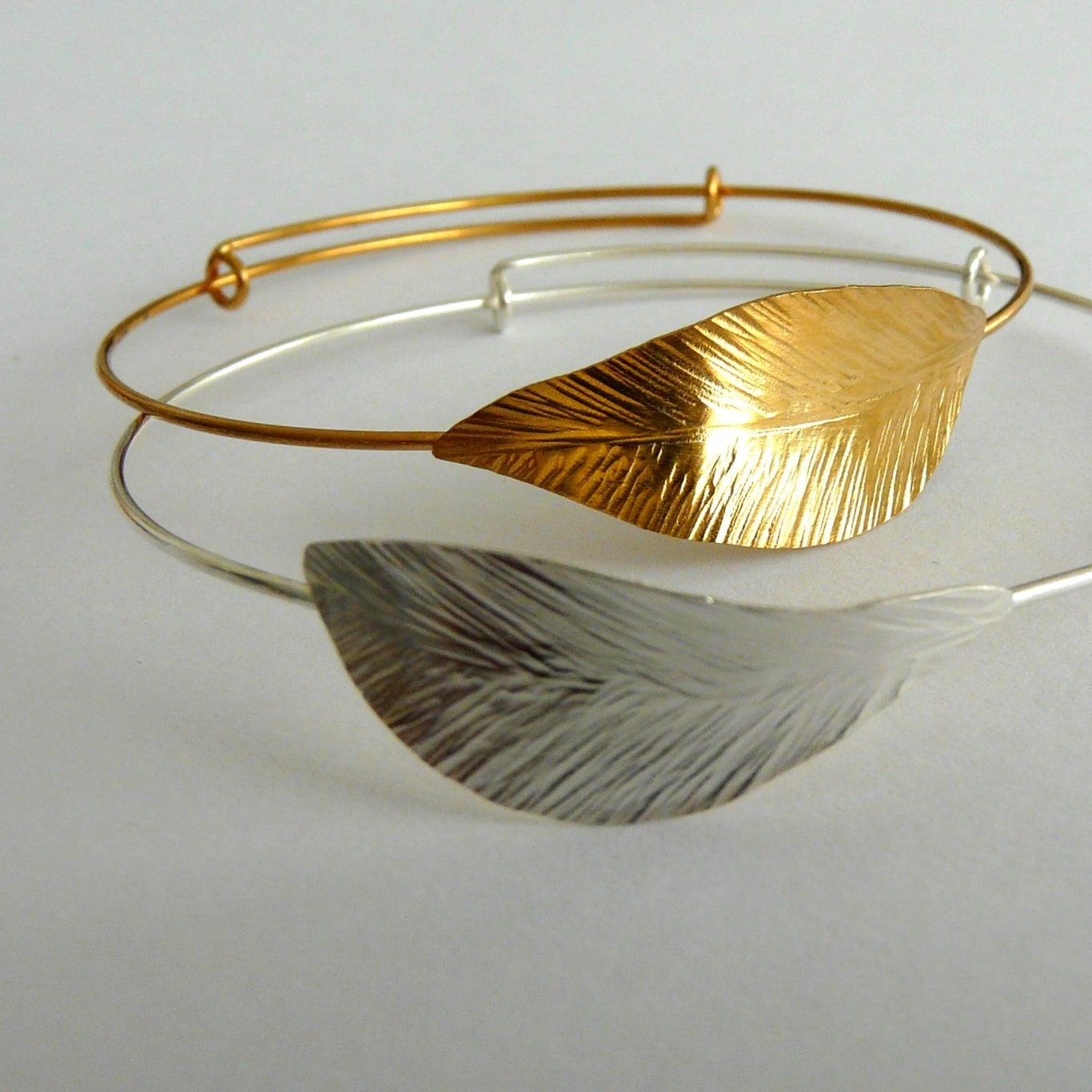 Gold and silver leaf-shaped bracelet on a light gray background