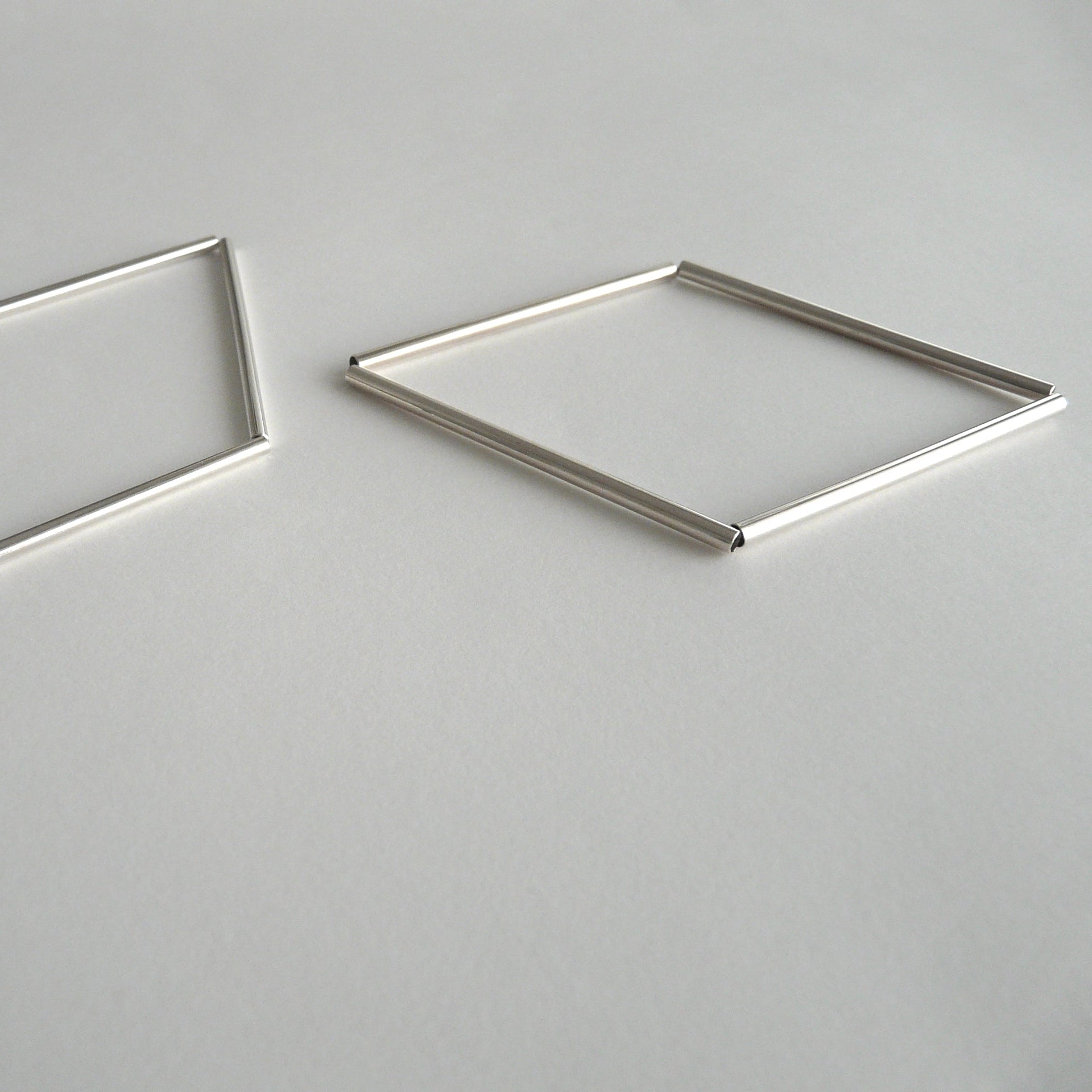 Two geometric metal earrings on a gray background
