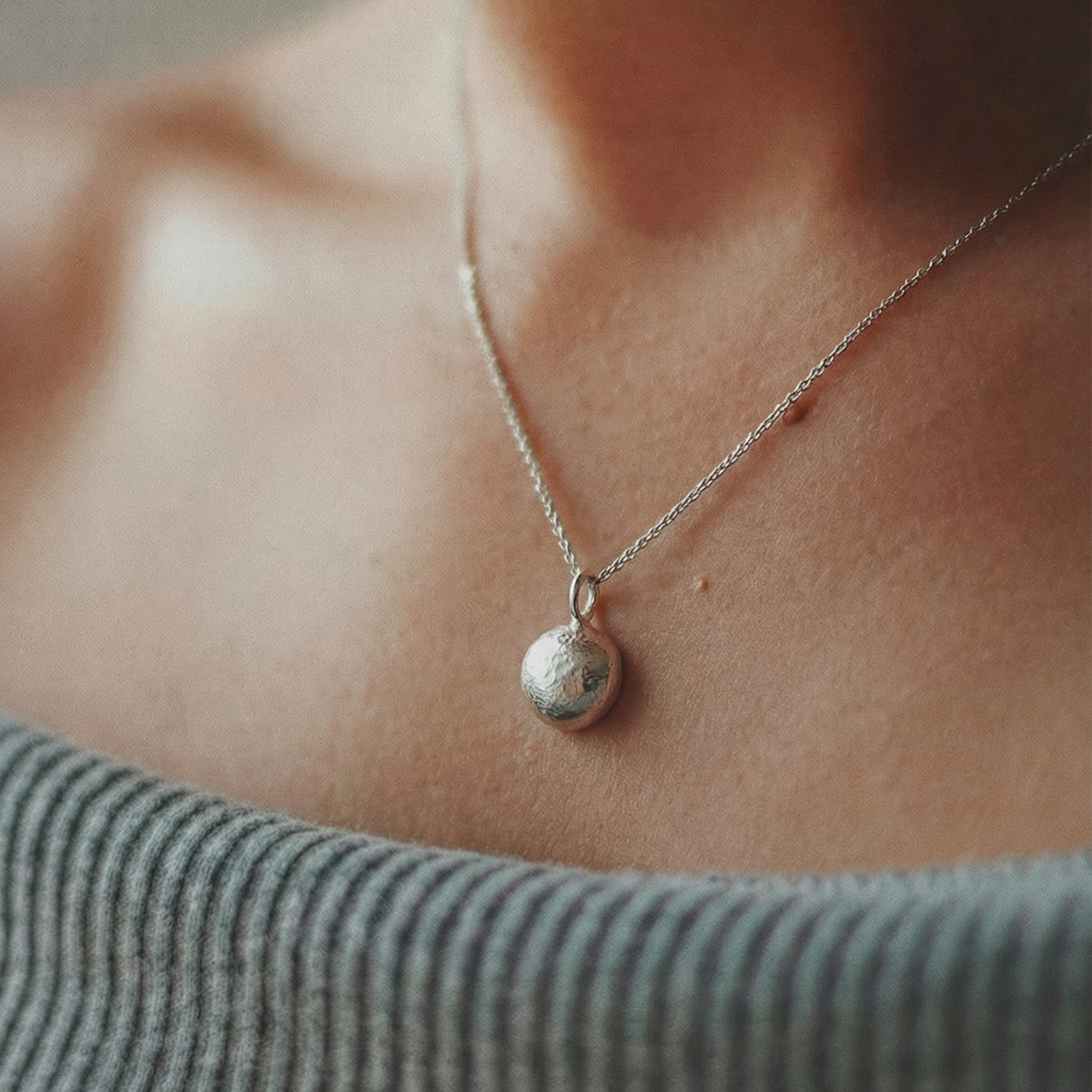 Close-up of a person wearing a silver necklace with a pendant.
