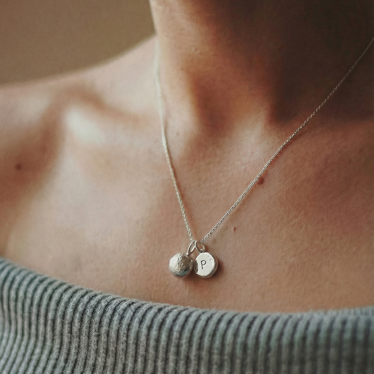 Necklace with round pendants on a person wearing a gray top.