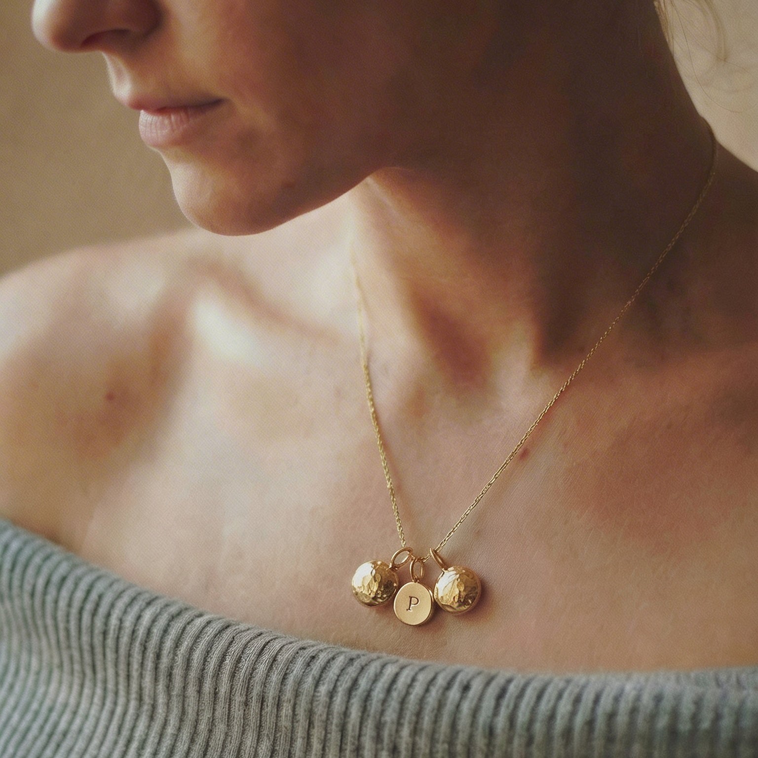 Woman wearing a gold necklace with circular pendants against a neutral background