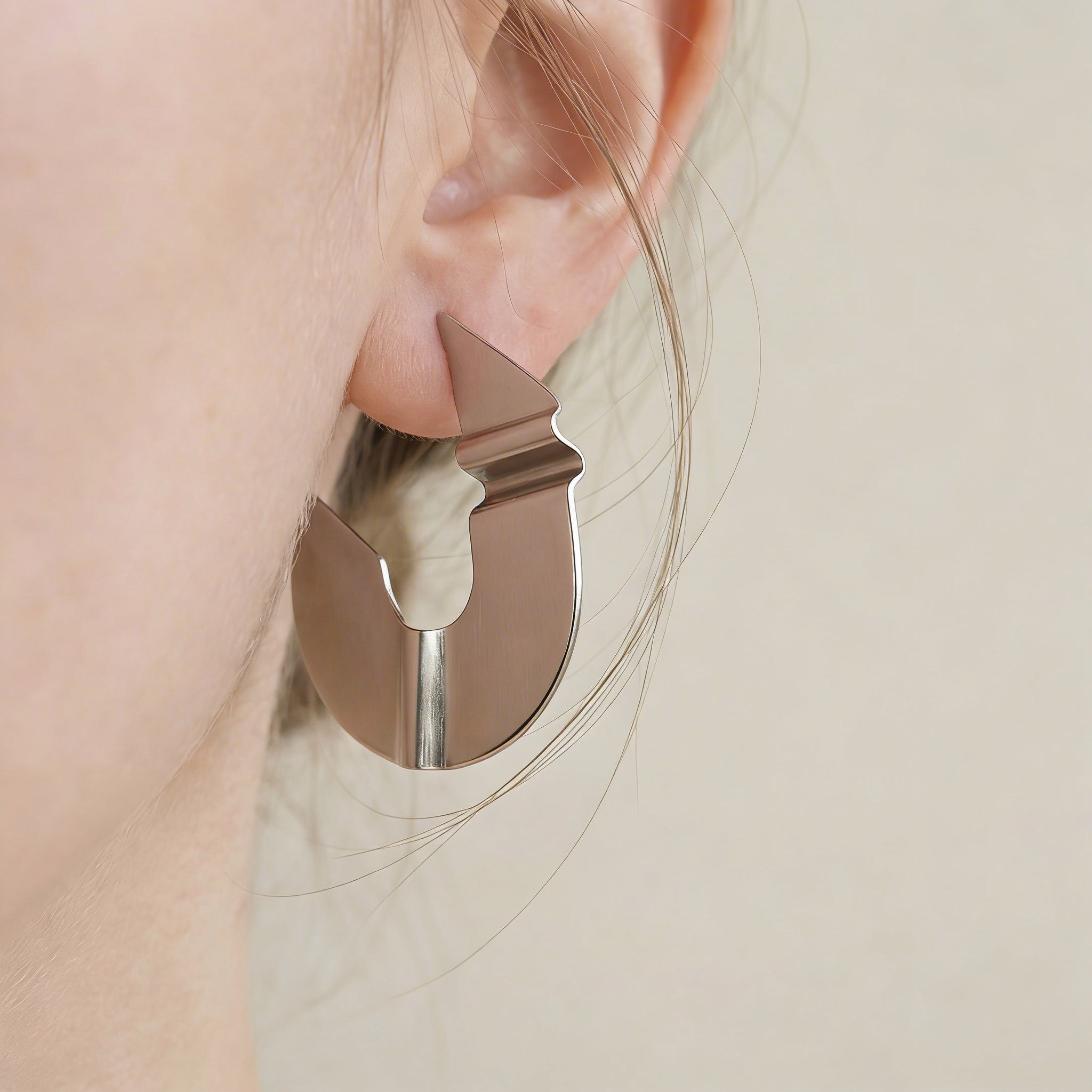 Close-up of a person wearing a silver geometric earring on a neutral background